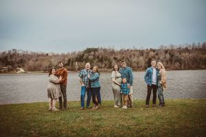 Group poses together in casual attire by a scenic lake on an autumn day.