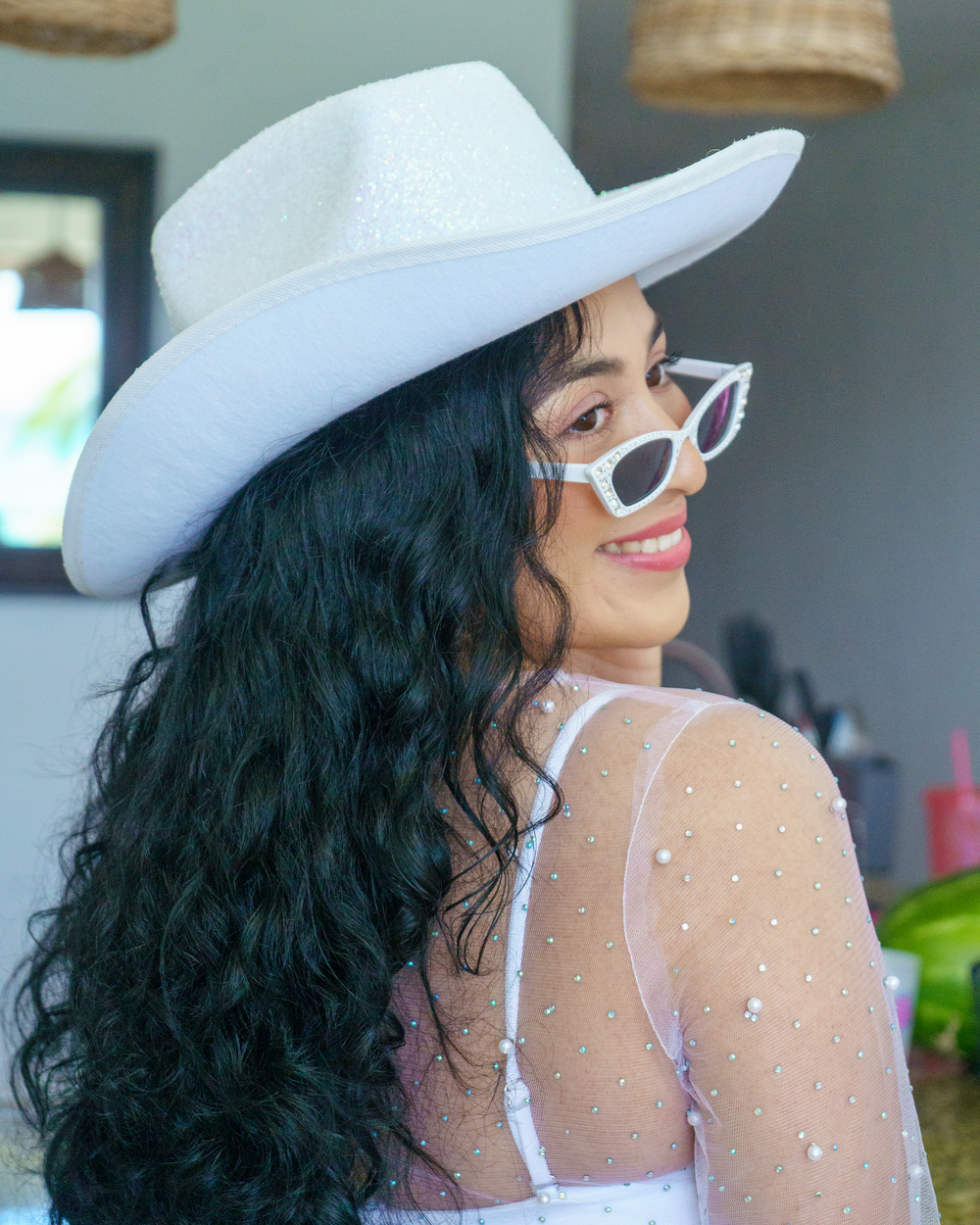 Person in white cowboy hat and sunglasses poses against blue interior backdrop.