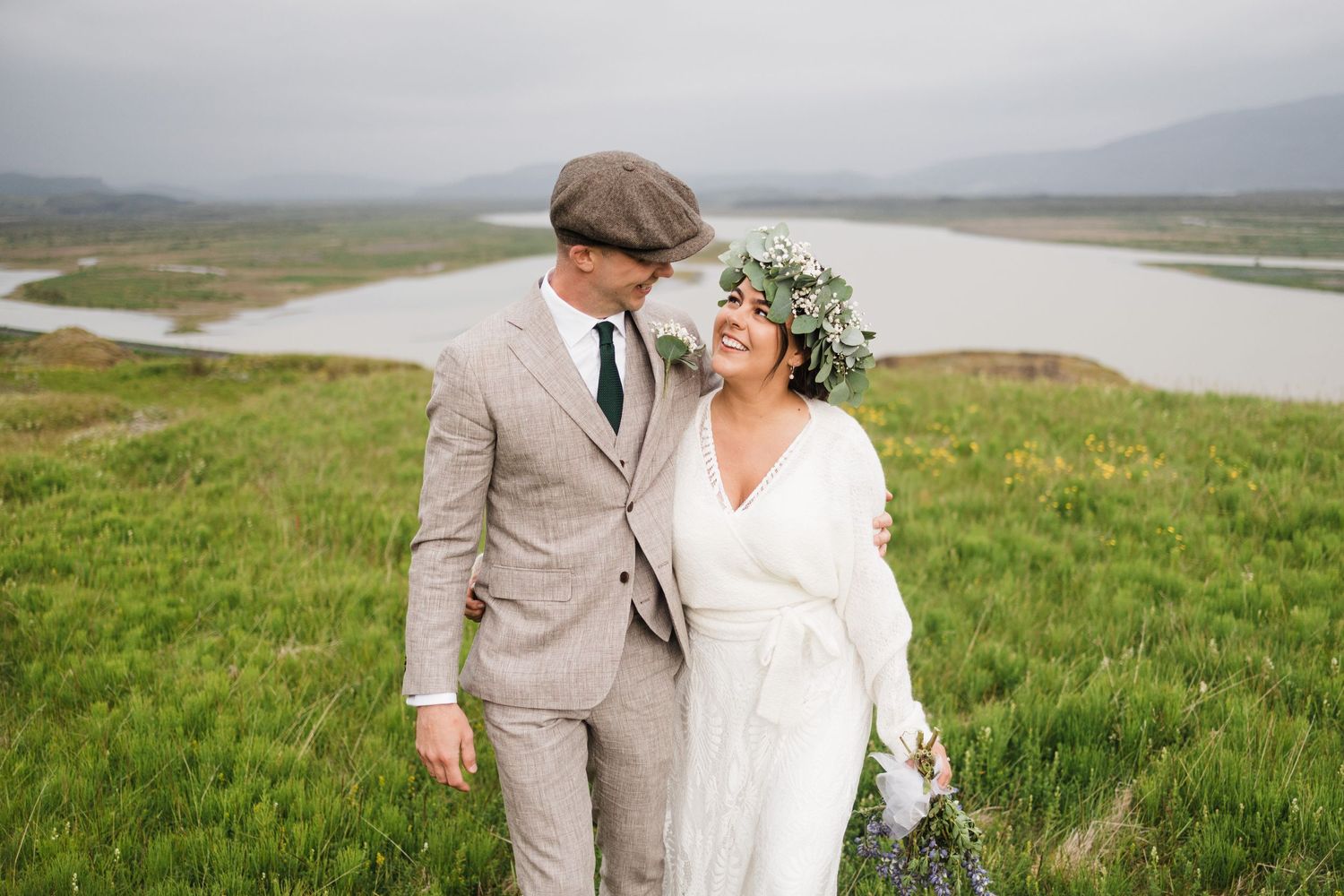 A wedding couple shares an intimate moment on a green hillside overlooking a winding river.