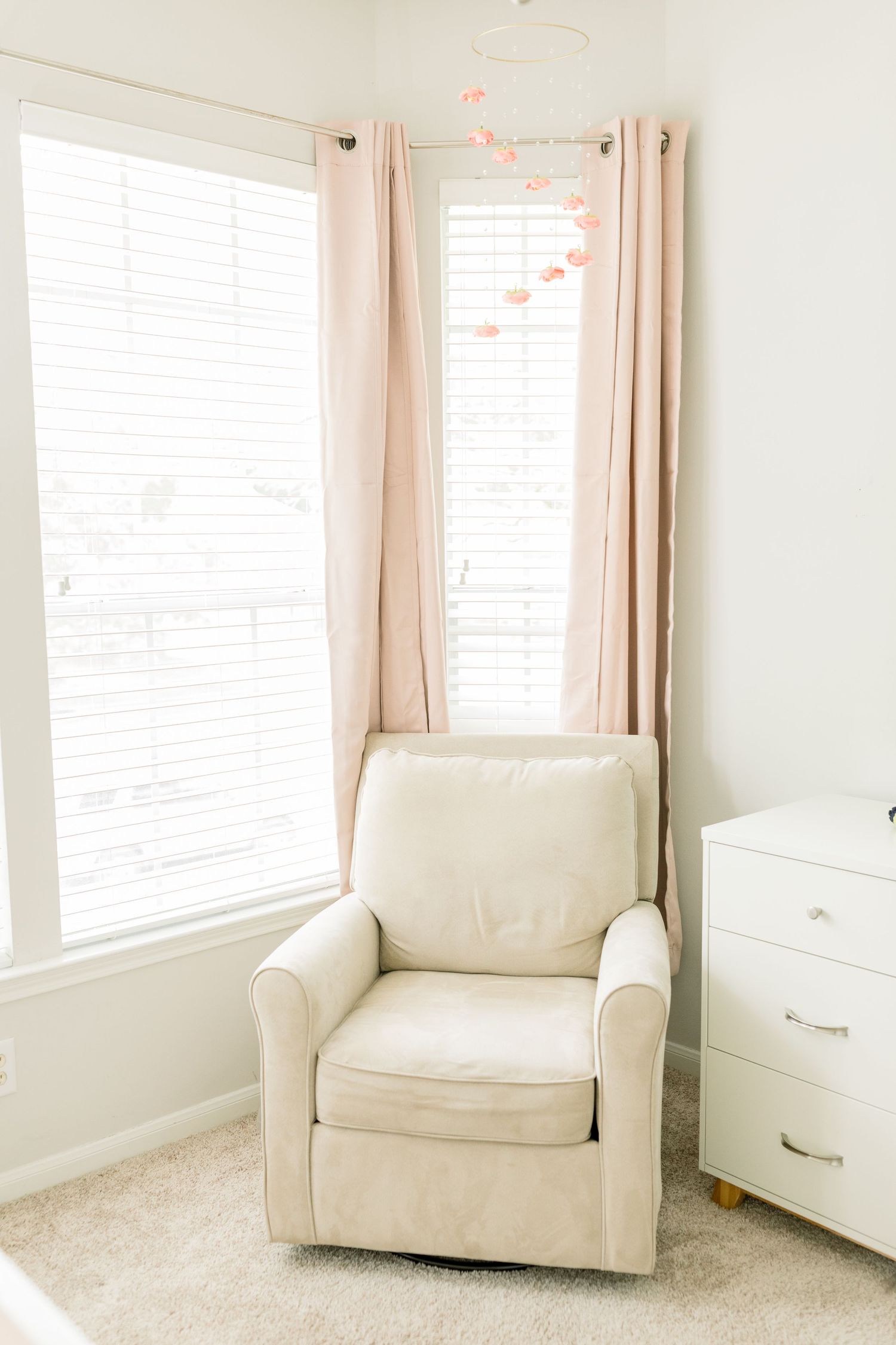 Minimalist nursery corner with beige armchair, white dresser, and blush curtains.