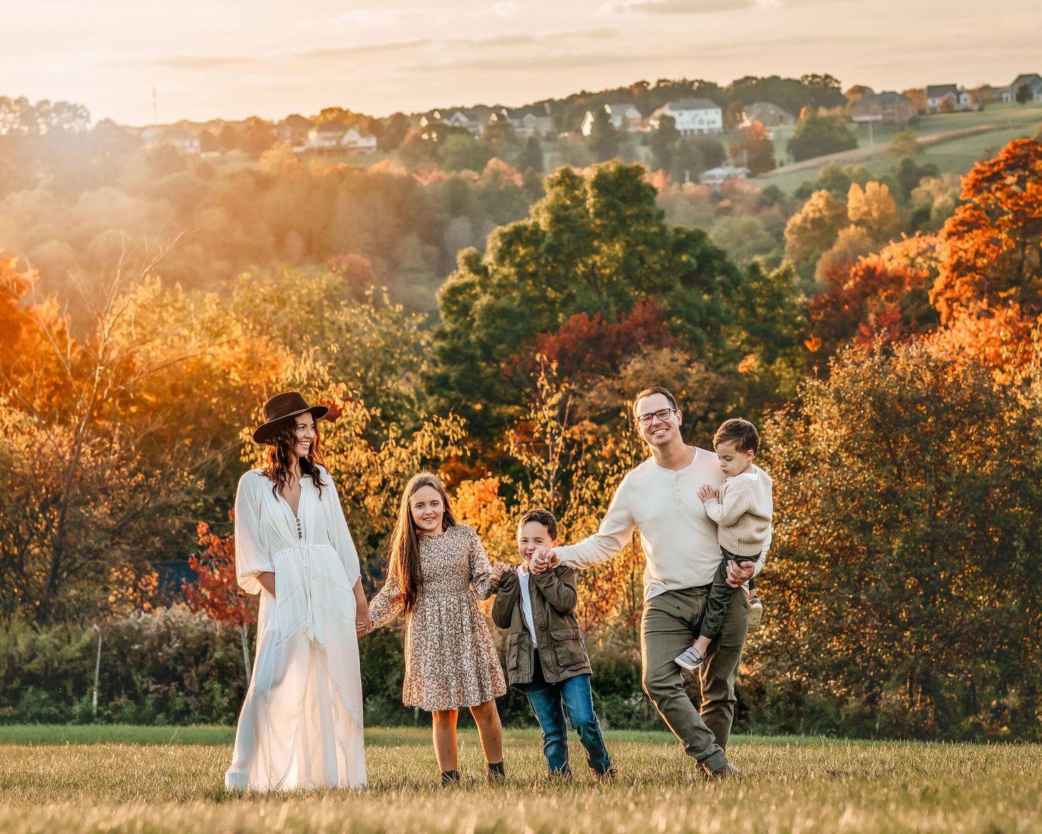 Happy family of five walks through golden autumn meadow at sunset with colorful fall foliage.