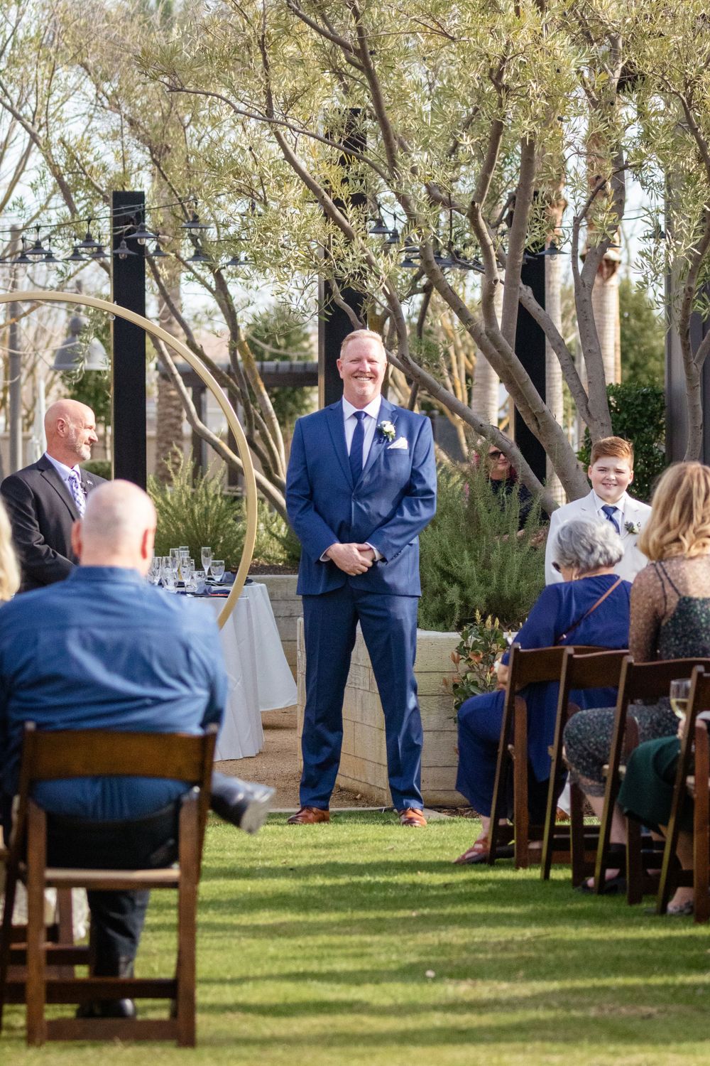 Wedding guests seated on wooden chairs during outdoor garden ceremony.