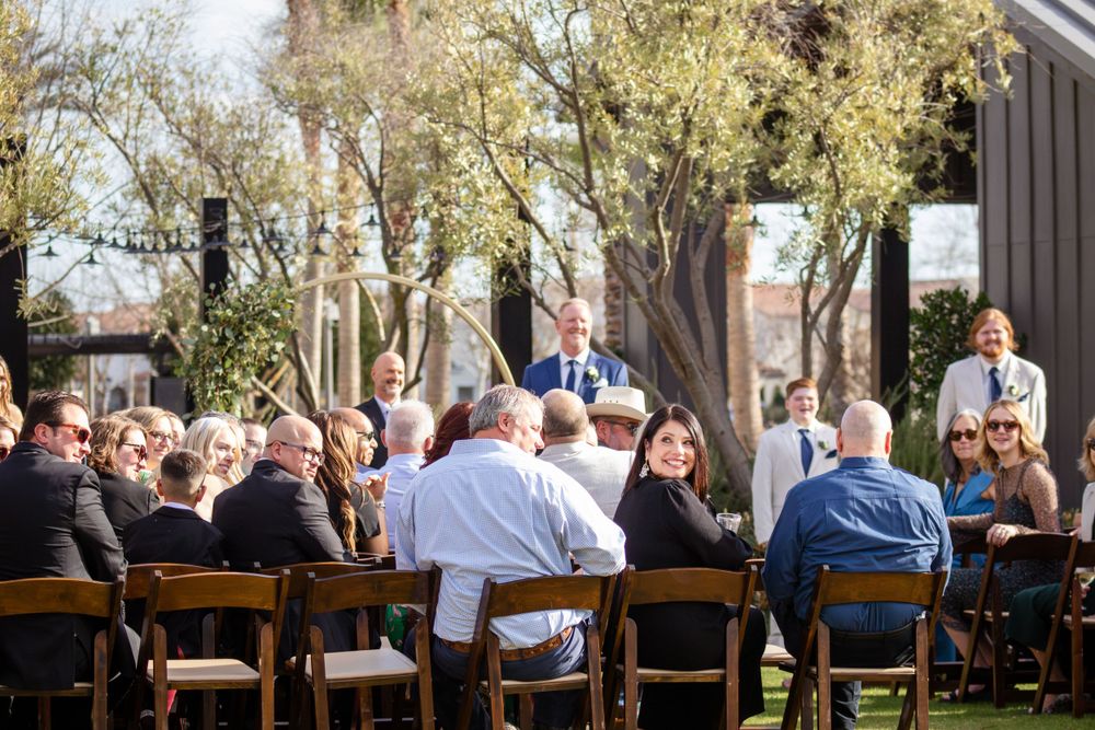 Wedding ceremony guests seated in rows of wooden chairs on a grassy lawn.