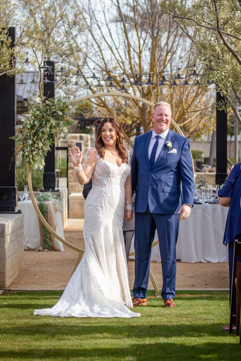 Couple walks down outdoor aisle after wedding ceremony with guests seated on both sides.