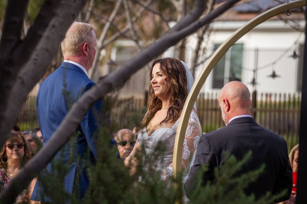Wedding ceremony taking place outdoors with trees and natural lighting.
