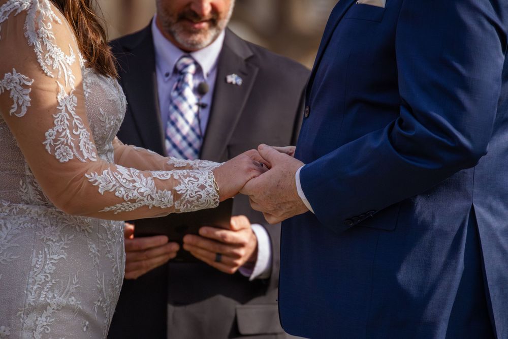 Close-up of hands exchanging wedding rings during outdoor ceremony.