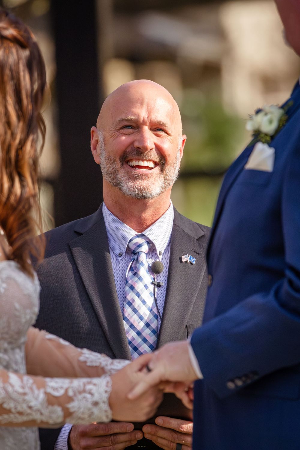 Wedding officiant in checkered tie conducts outdoor ceremony.