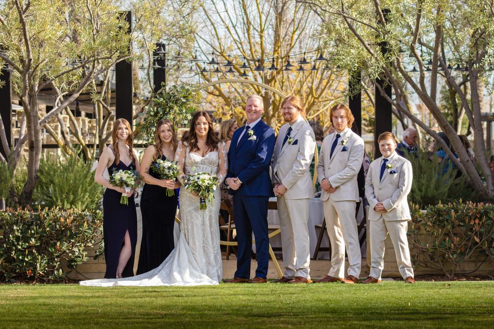 Wedding guests gathered outdoors in formal attire on a sunny day.