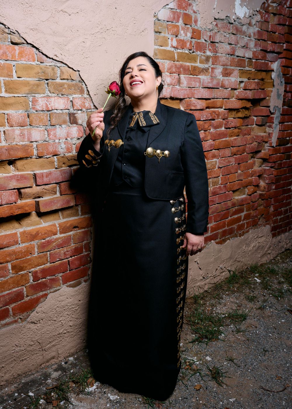 Person in traditional mariachi attire smiles while holding red rose.