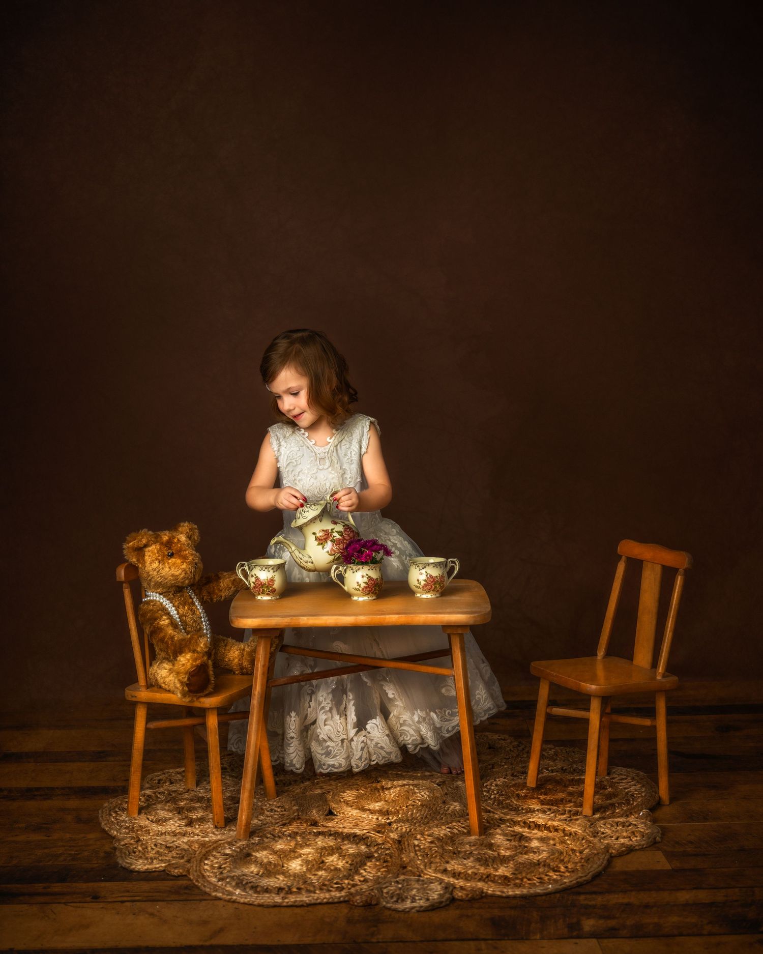 Whimsical tea party setting with stuffed bear guest and vintage wooden furniture on dark background.