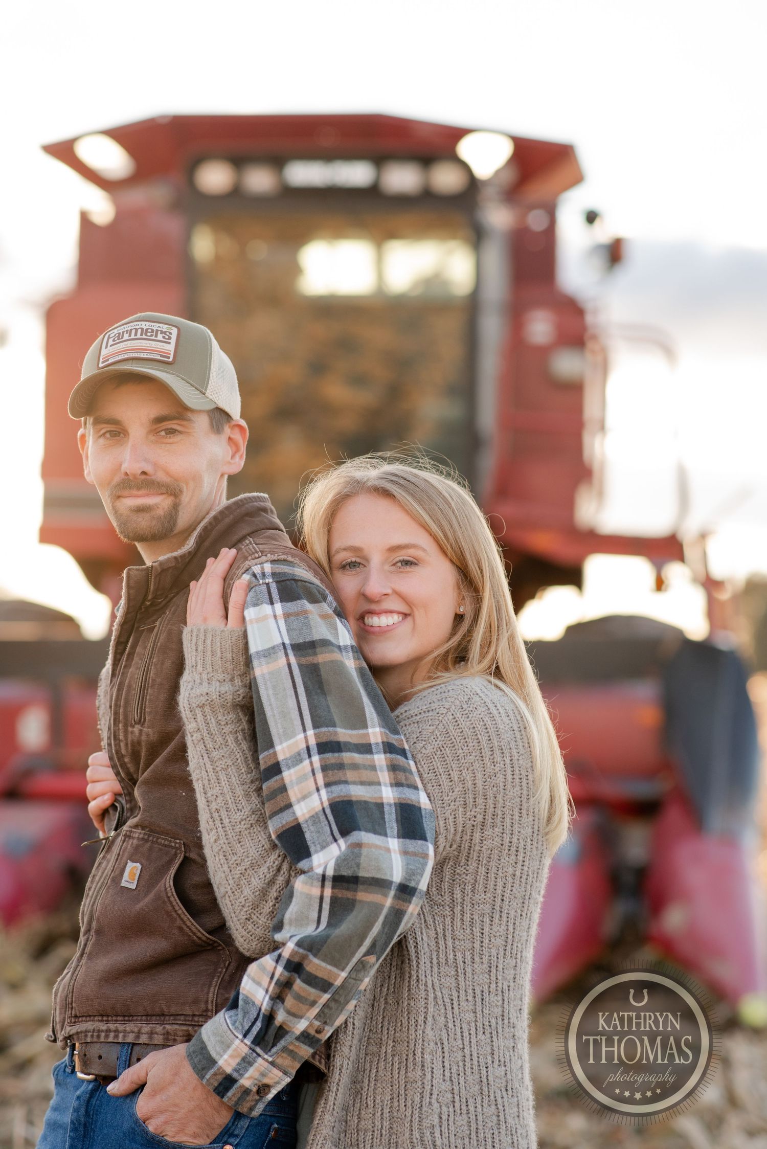 Couple embracing in front of red combine harvester during harvest season.