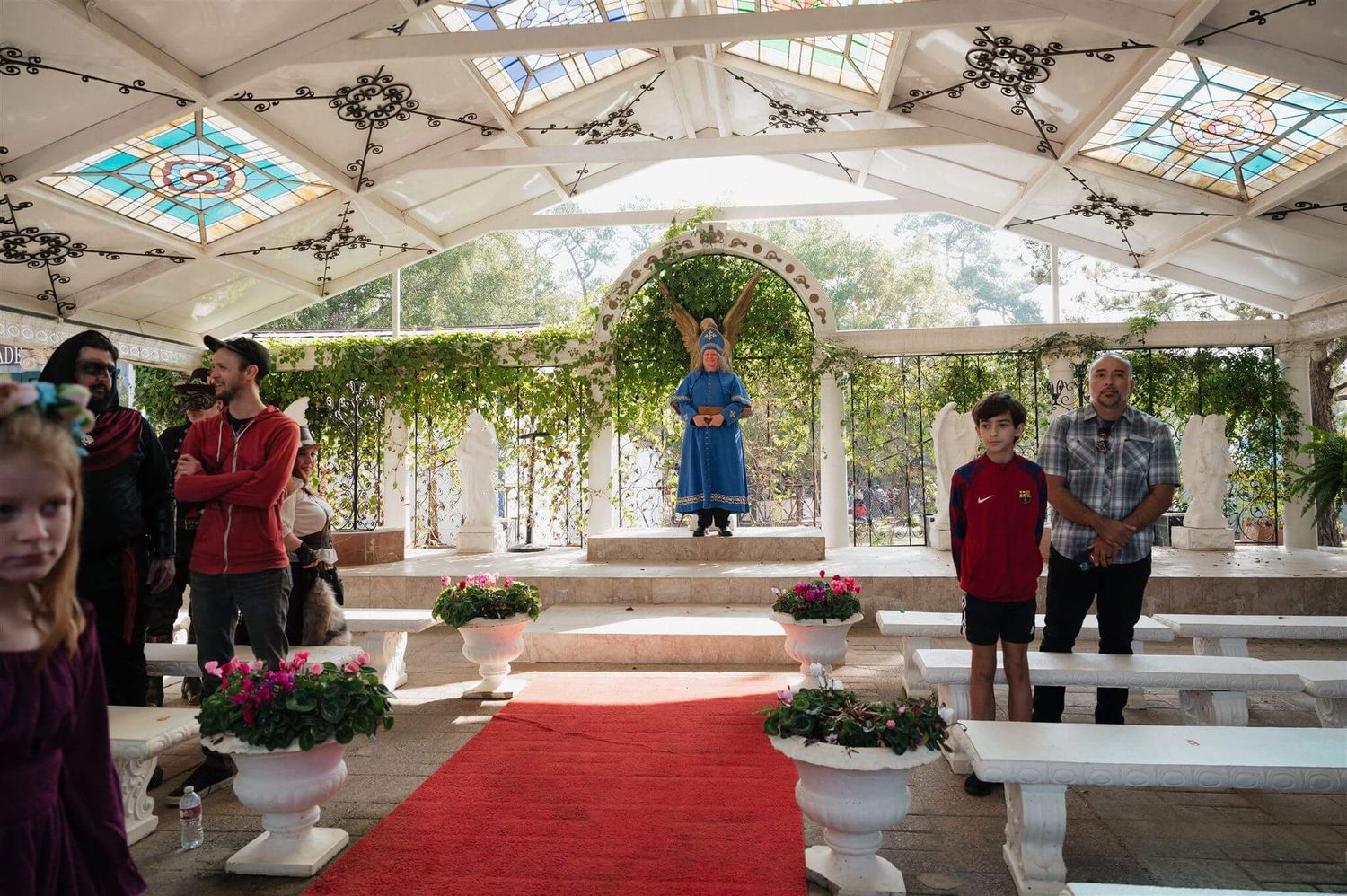 An indoor wedding ceremony space with white benches and floral decorations under a skylit canopy.