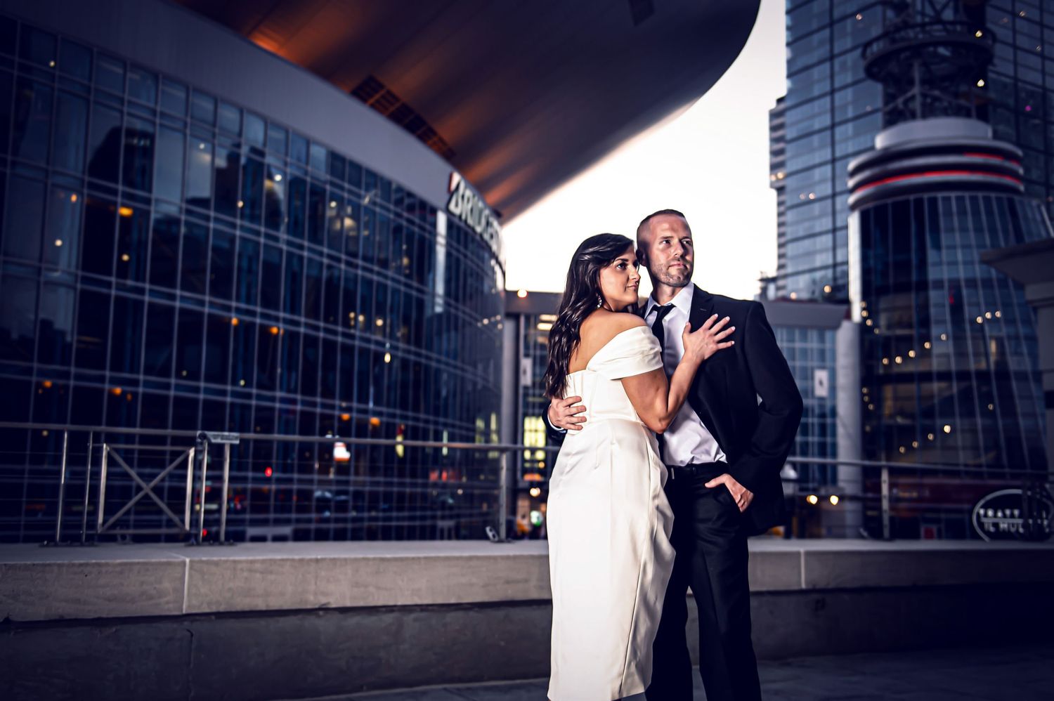 Dramatic nighttime wedding portraits outside modern glass building with city lights.