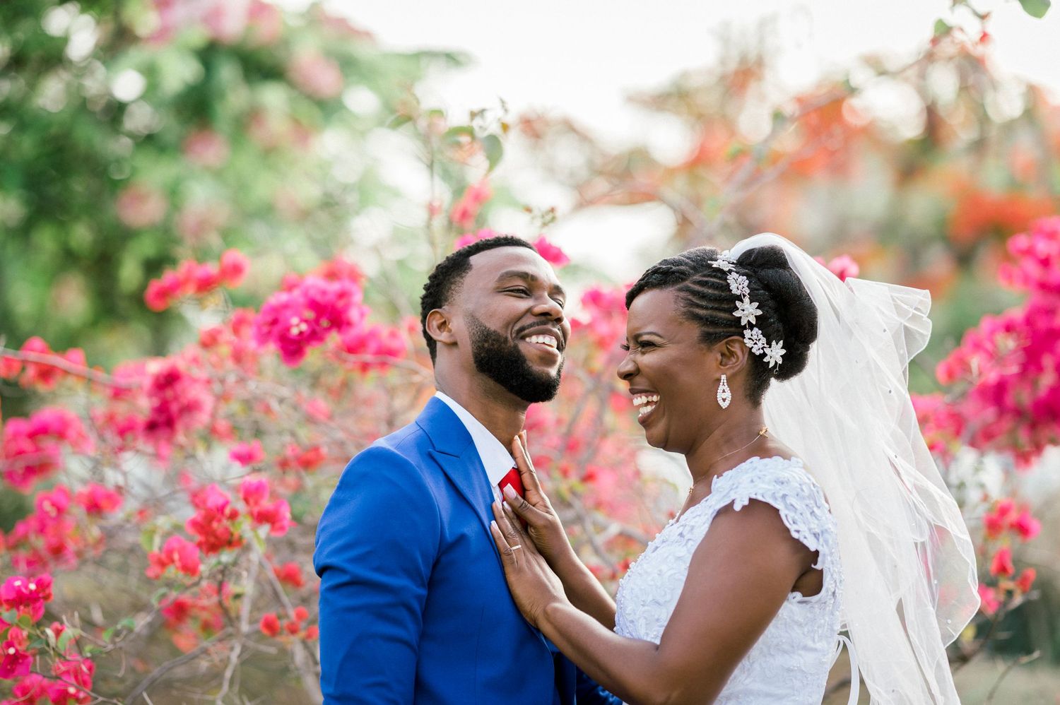Mariés en Martinique, le couple est de profil souriant tous les deux devant un massif de fleurs roses
