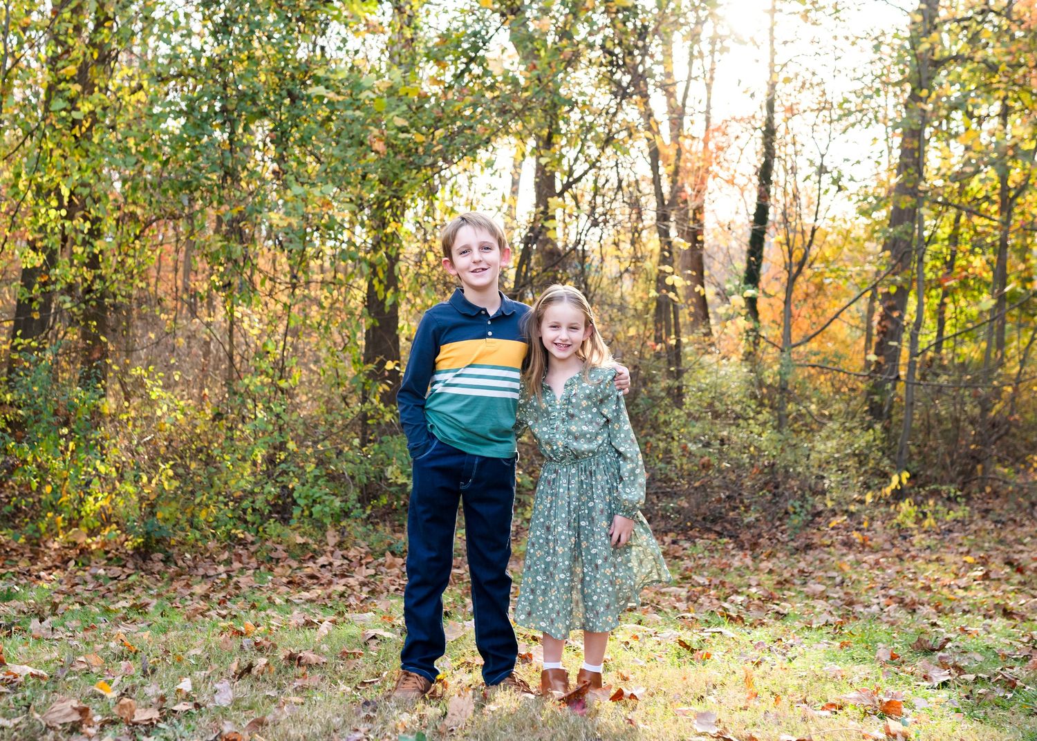 Family sits together on fallen log surrounded by colorful autumn forest leaves.