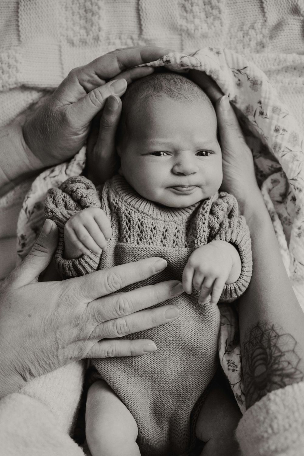 Black and white portrait of a small baby in knit sweater being held by caring hands.