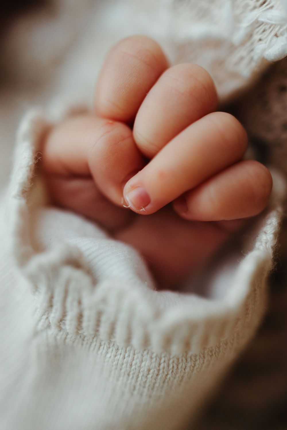 Close-up macro shot of tiny baby fingers wrapped in soft white knitted fabric.
