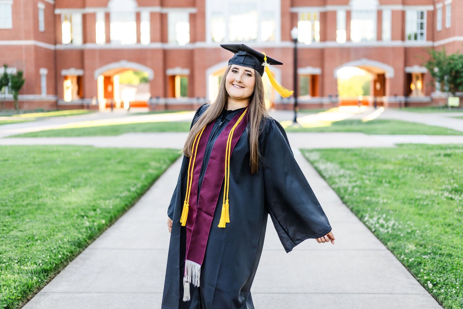 Graduate smiles while posing in traditional cap and gown on campus.