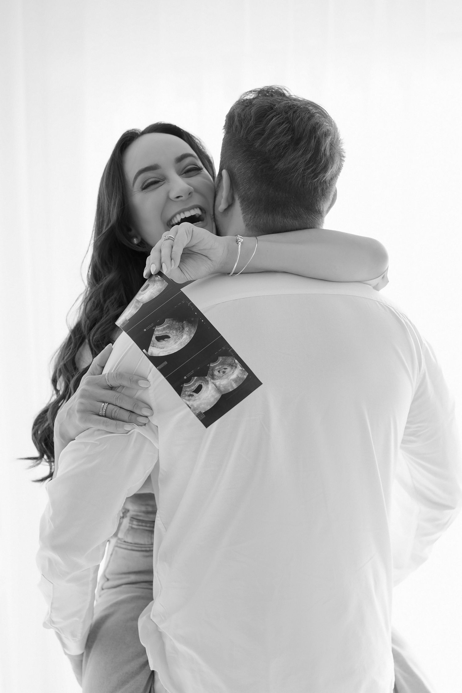 Joy-filled moment captured in black and white as couple holds ultrasound photo.
