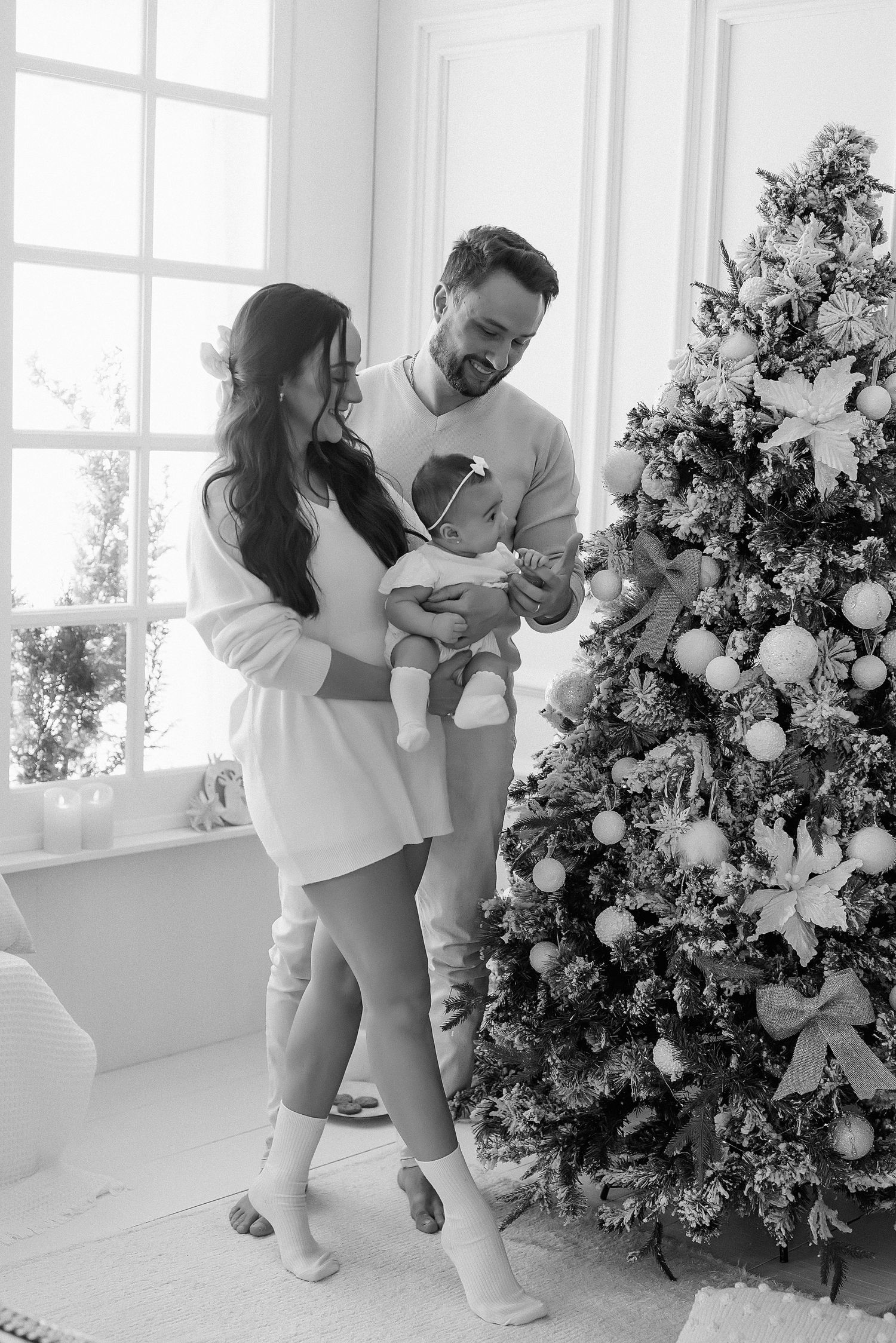 Family celebrating first Christmas together by decorated tree in bright white room.