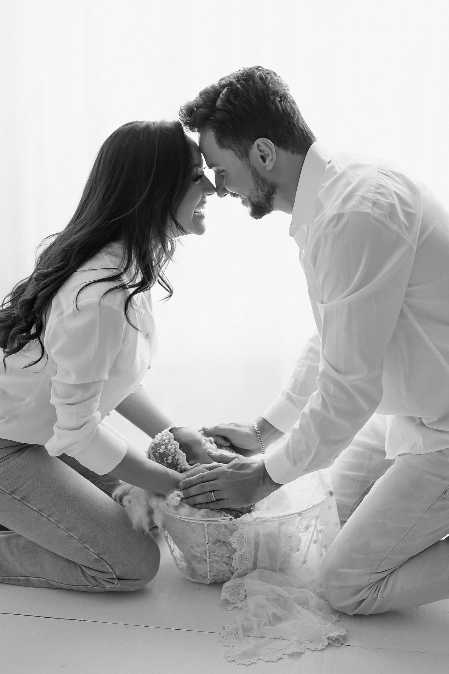 Intimate black and white photo of couple touching foreheads in tender moment on white background.