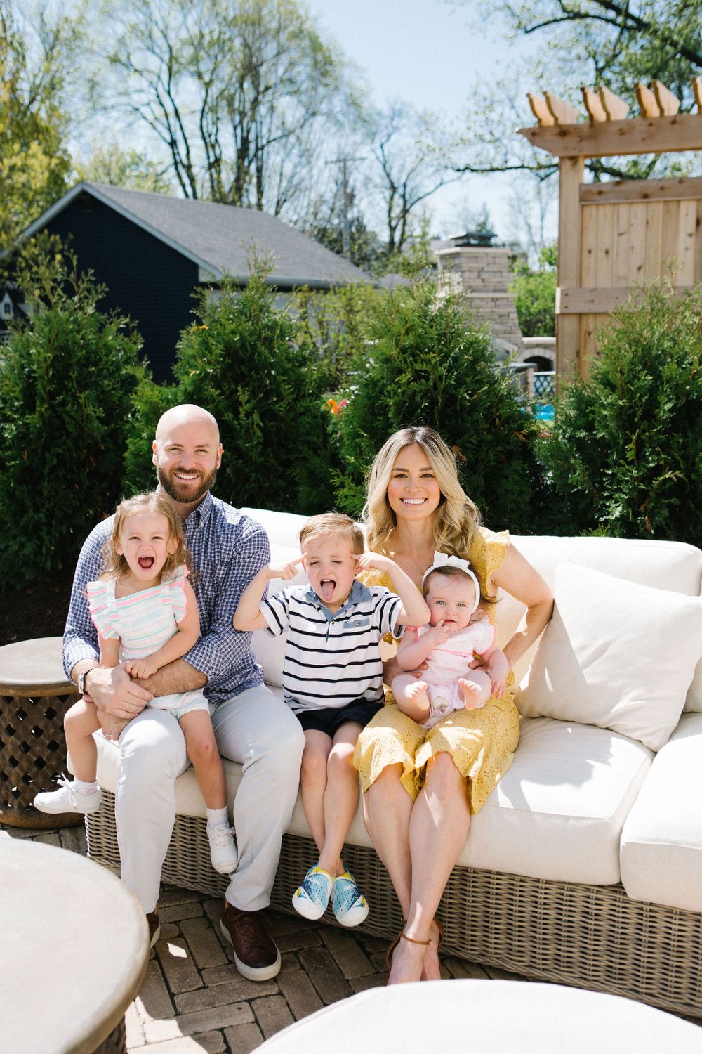 Happy family of five with three young children posing together on outdoor patio furniture in spring.