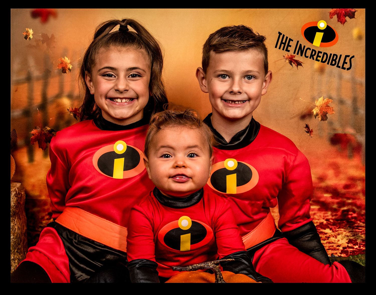 Three children in matching red Incredibles costumes pose for fall themed family photo.