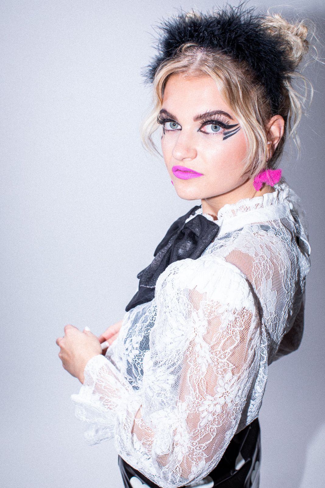 Editorial fashion shot showcasing dramatic makeup and a white lace blouse with black bow detail.