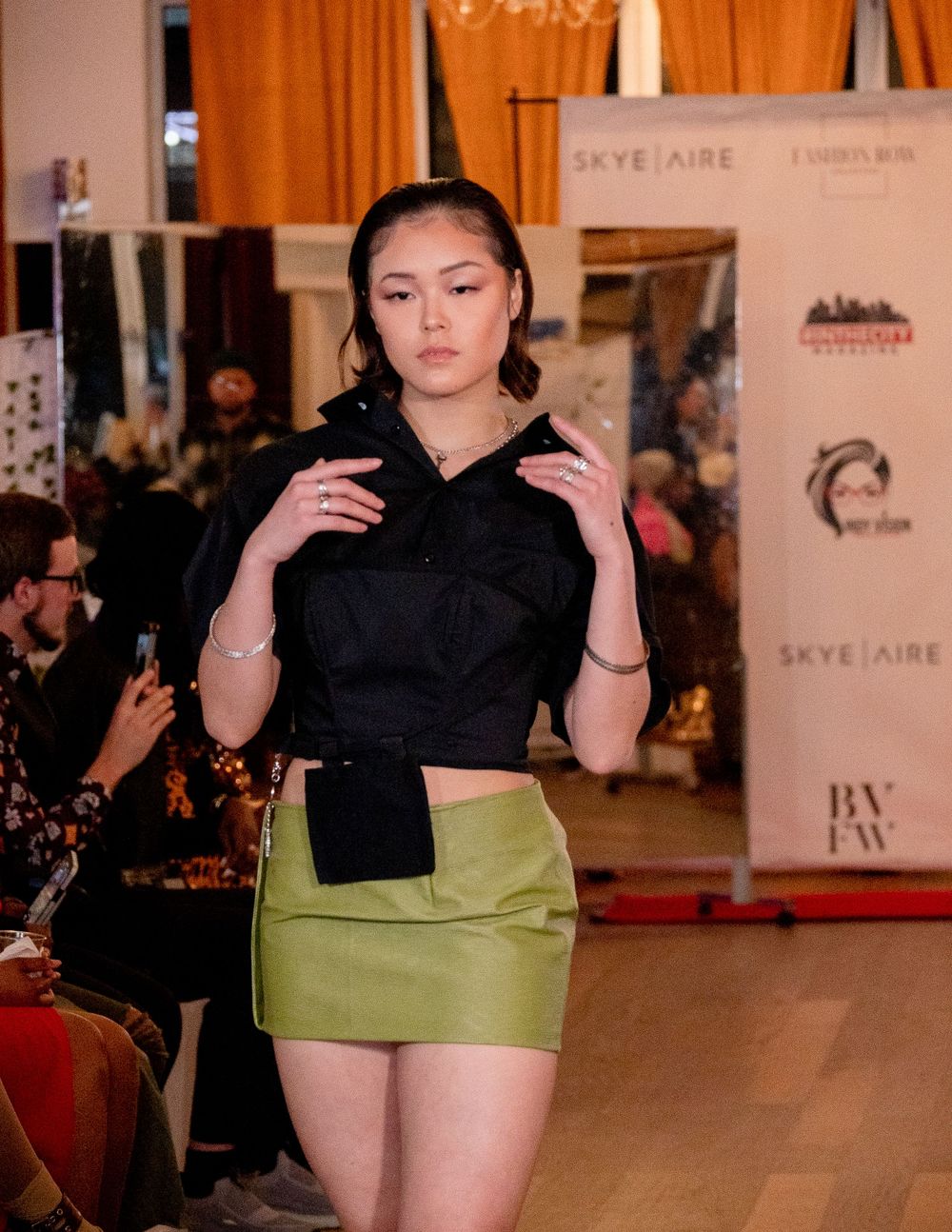 Fashion model presents black crop top and lime green skirt on catwalk.