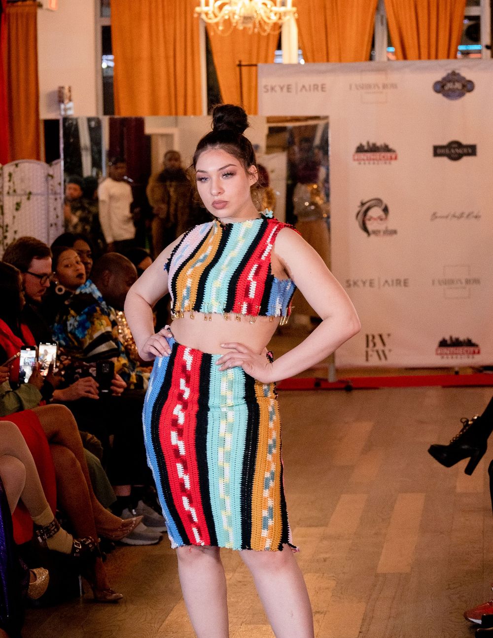 Model wearing colorful striped dress poses confidently on fashion runway.