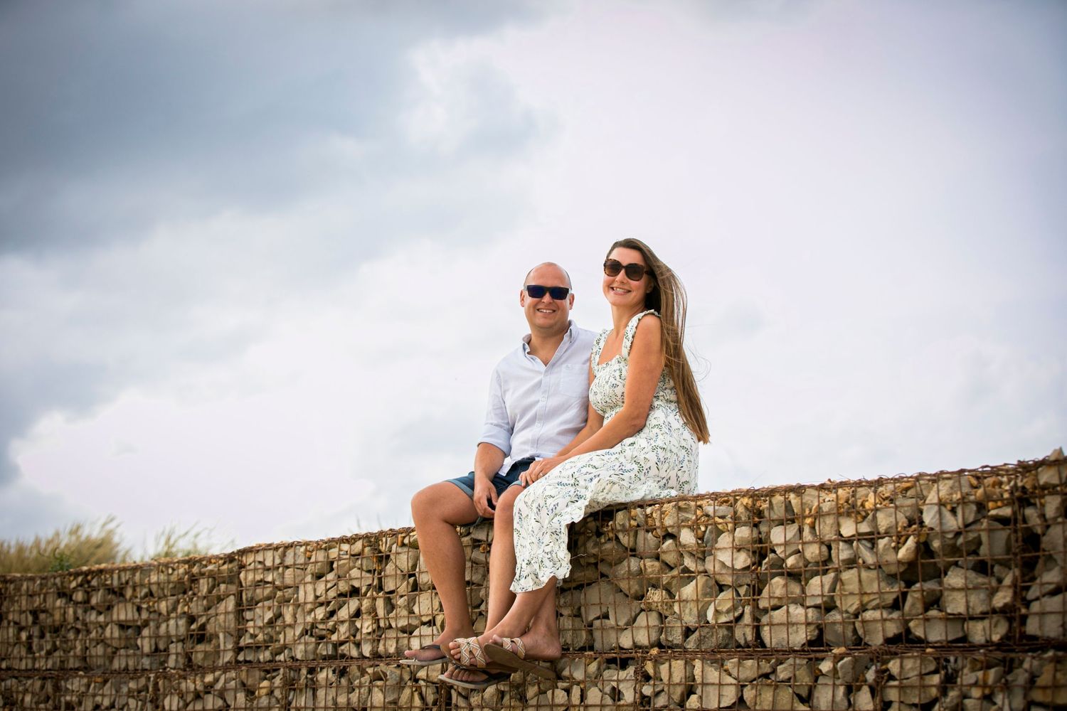 Two people embrace while standing on an ancient stone wall overlooking a scenic view.
