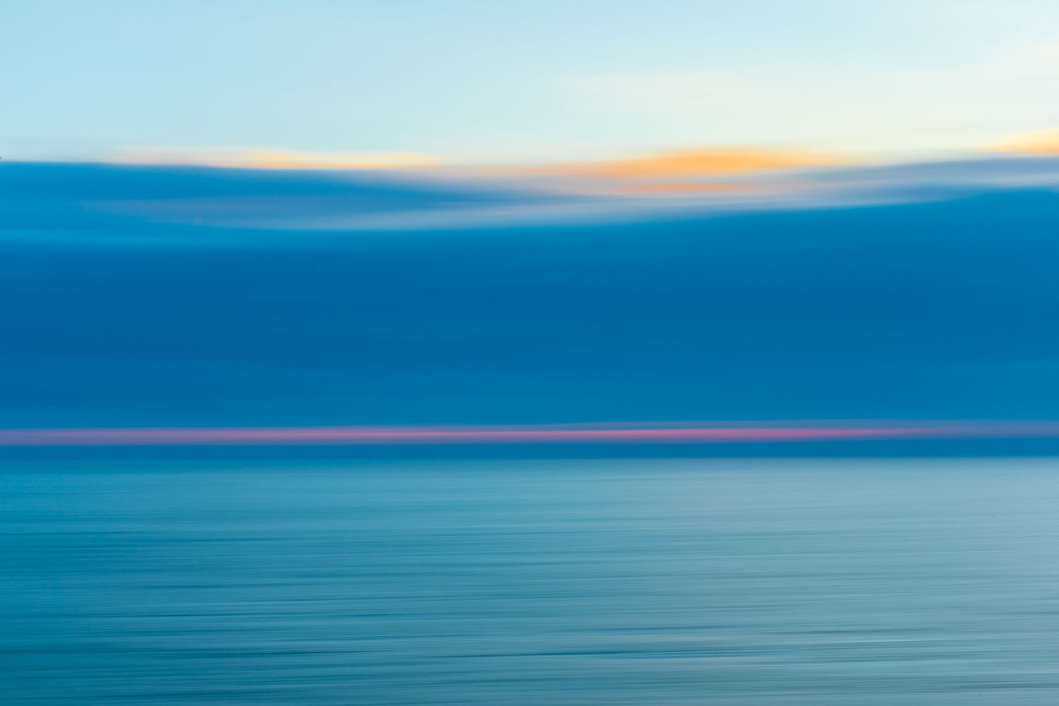 Abstract seascape with blurred motion creating bands of blue and turquoise colors at sunset.