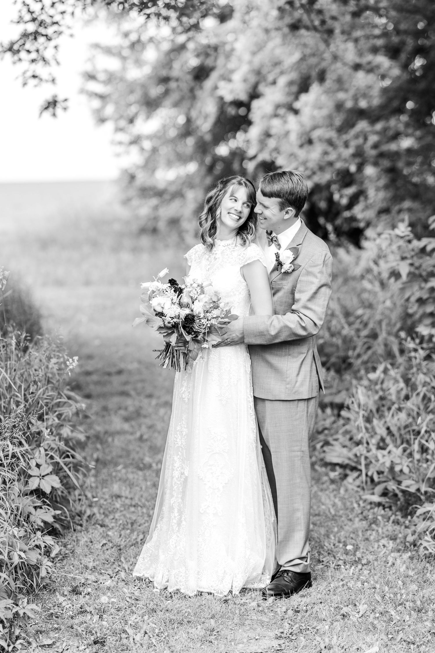 A black and white wedding portrait capturing an intimate moment between newlyweds outdoors.