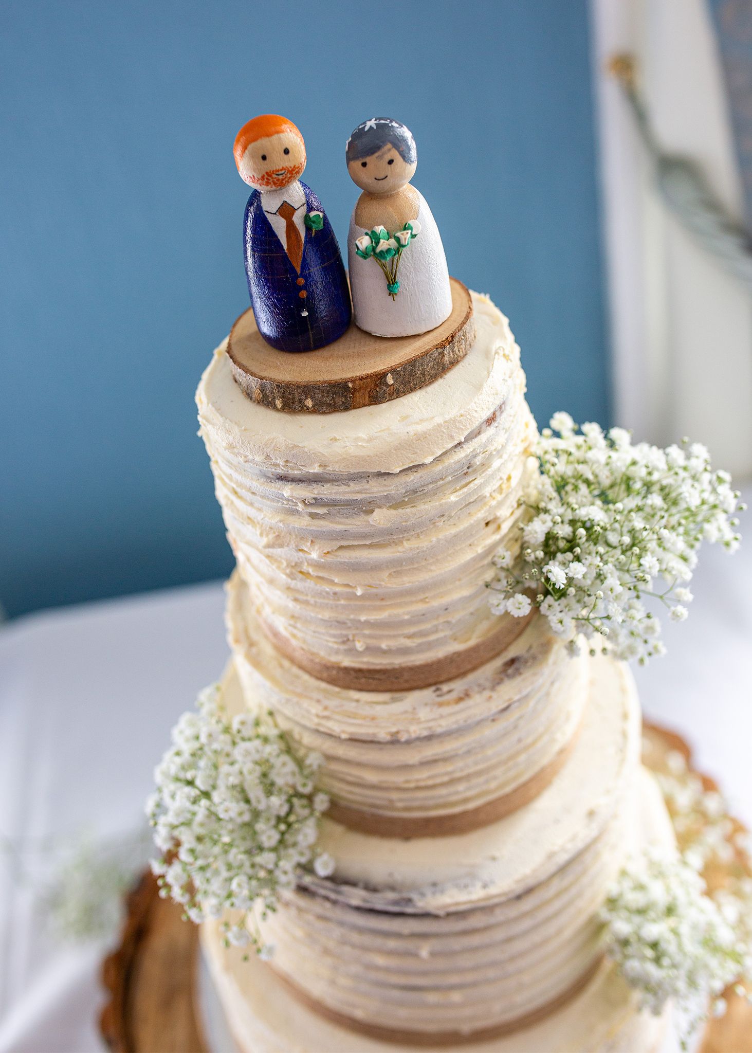 Three-tiered white wedding cake decorated with baby's breath flowers and custom wooden cake toppers.