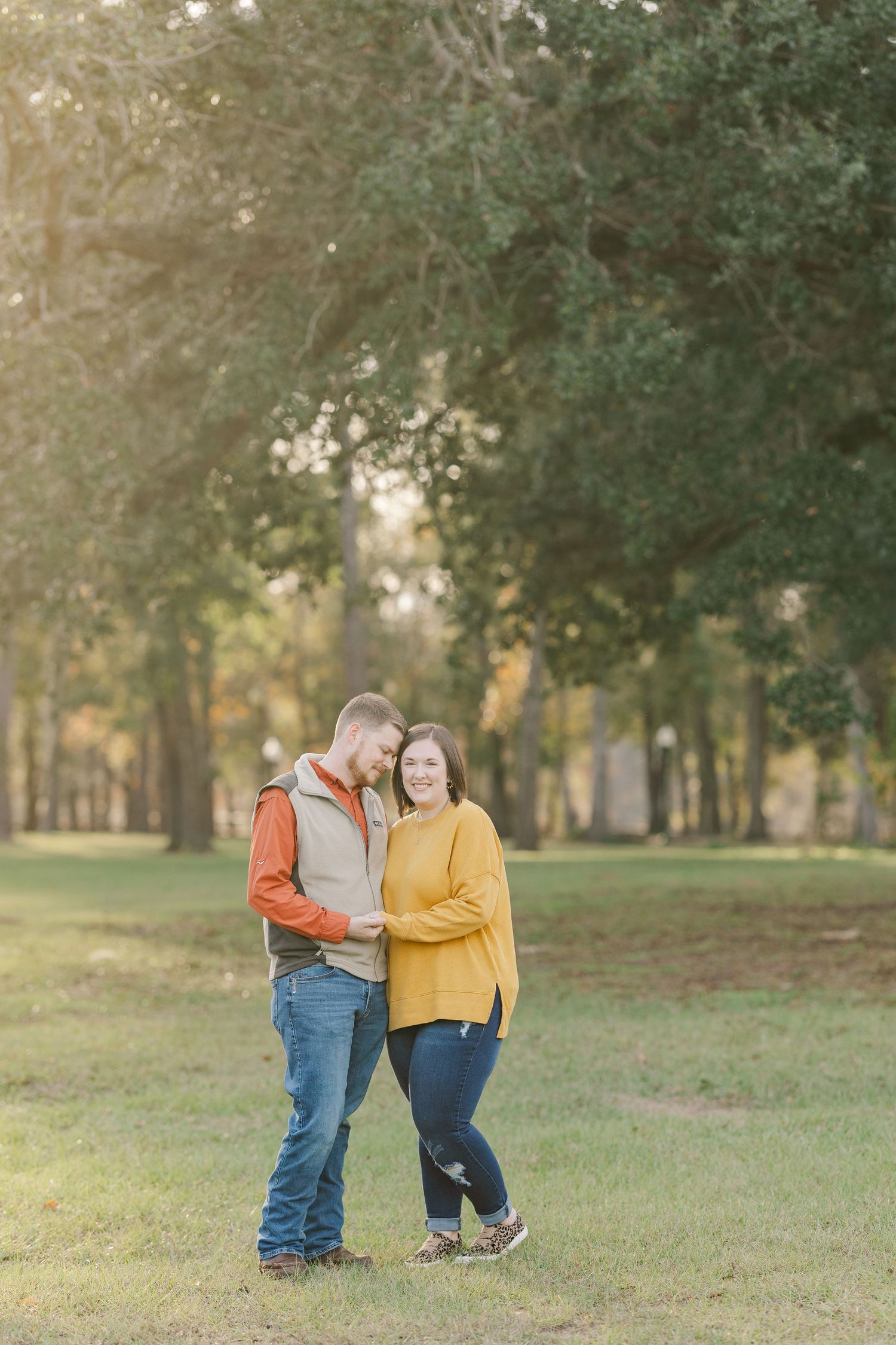 Couple in casual fall attire embracing in peaceful wooded park setting.