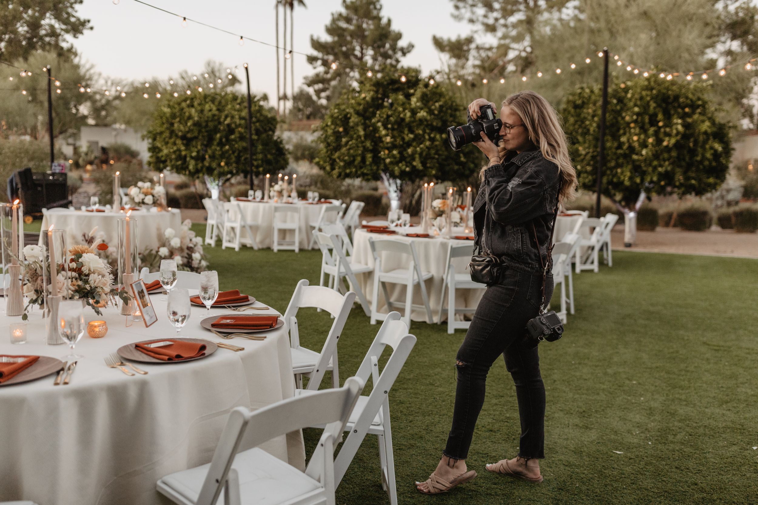 An outdoor wedding reception setup with white tables and chairs on a manicured lawn at dusk. Arizona wedding photographer. The Andaz
