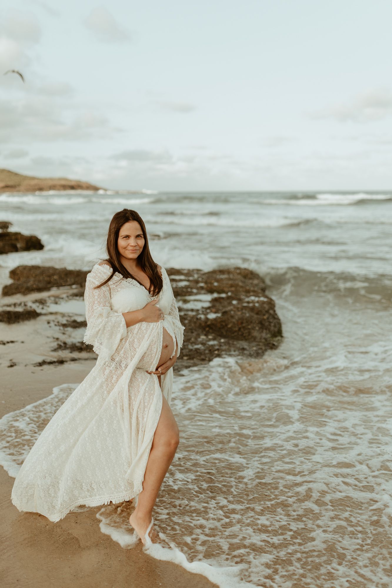 Maternity photo on beach with waves lapping at bare feet.