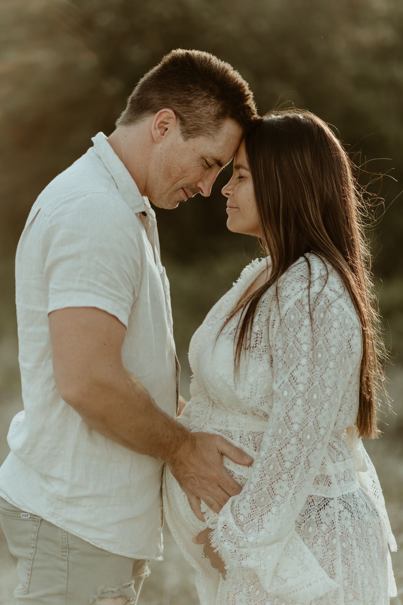 An intimate moment between a couple in white clothing during sunset.