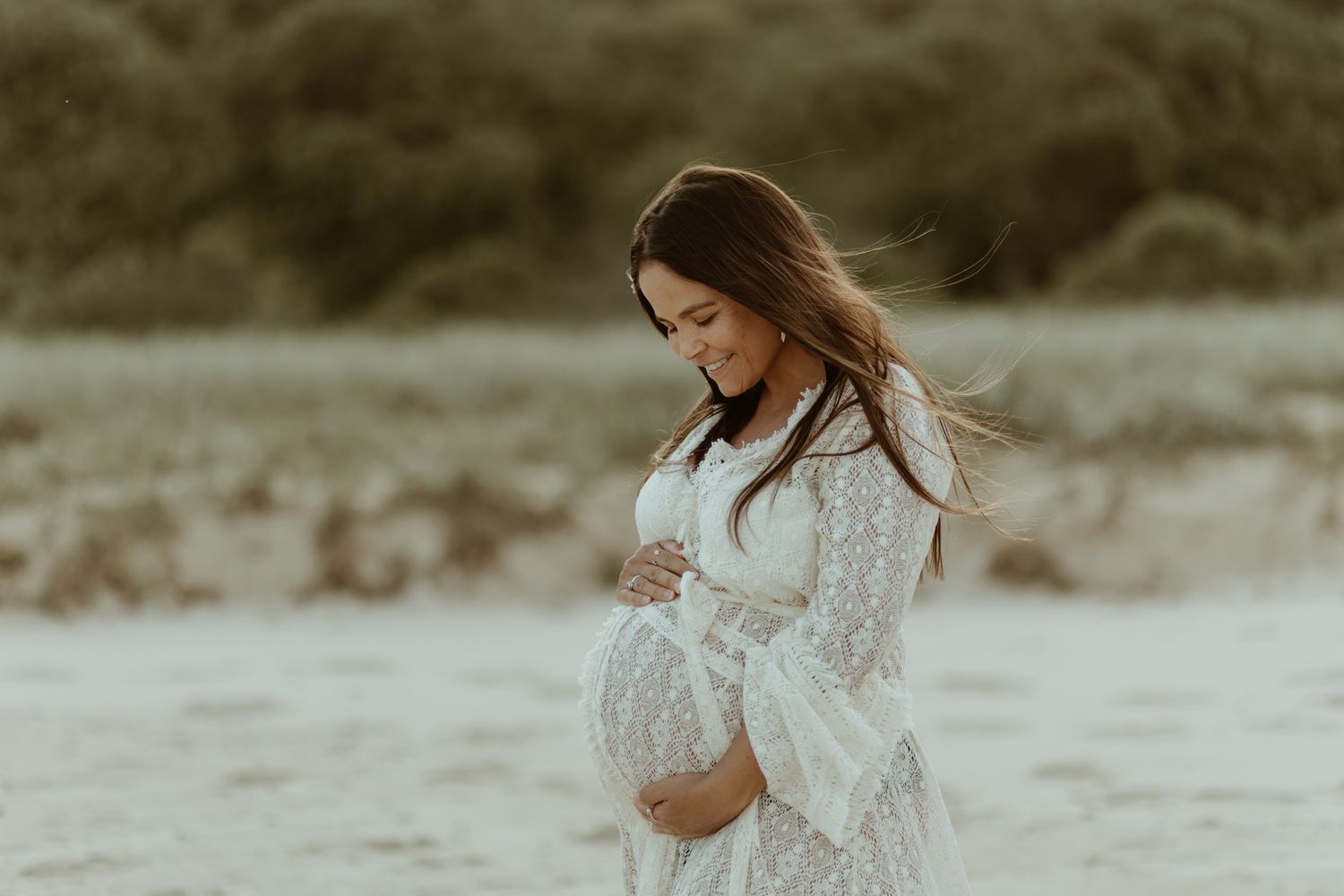 Ethereal maternity photo in white lace dress during golden hour.