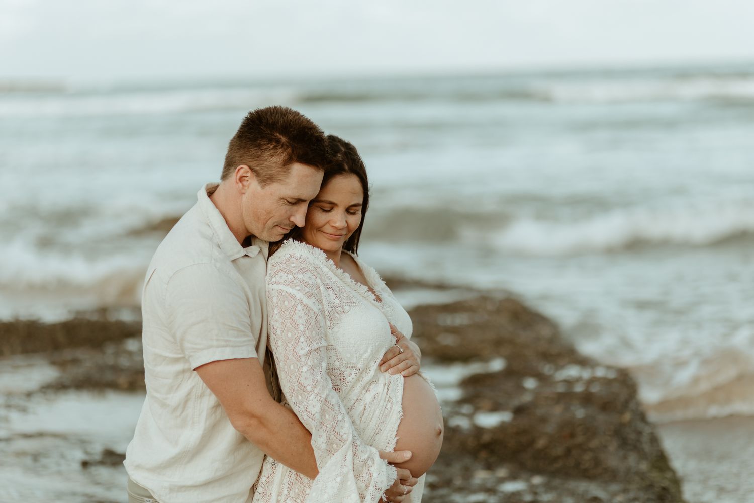 Romantic beachside moment with couple in white against ocean waves.