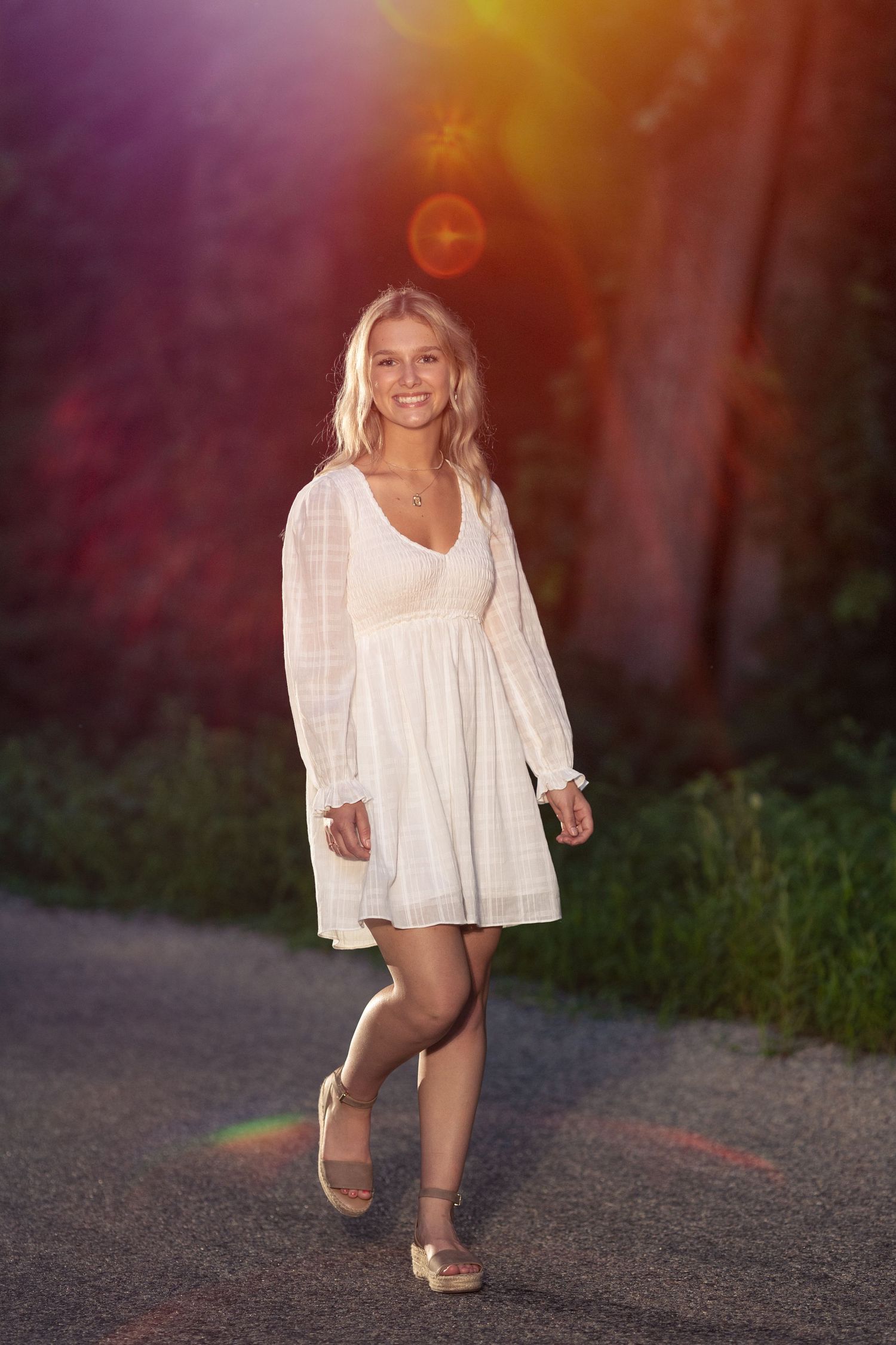 High school senior girl walking down a side road near Martinsville at sunset wearing flowing white dress.