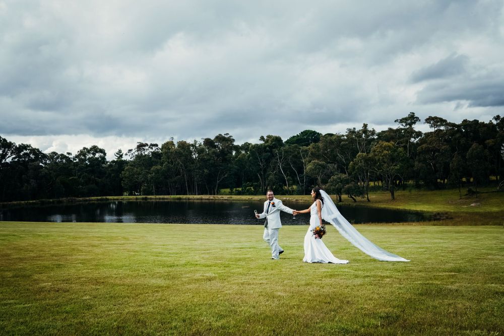 A rustic outdoor wedding setting under dramatic cloudy skies with white chairs on green grass.