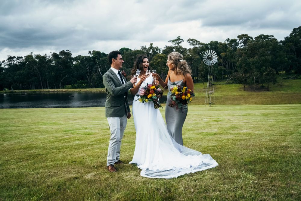 Wedding party gathered on a lush green field against cloudy sky backdrop.
