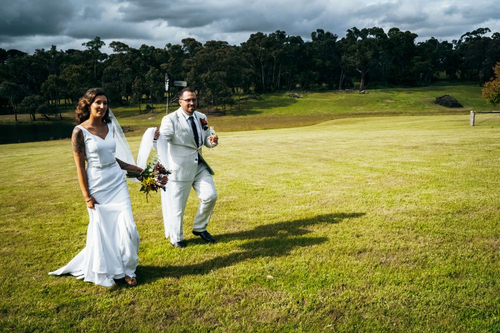 Wedding party runs playfully across a green field with mountains in the background.