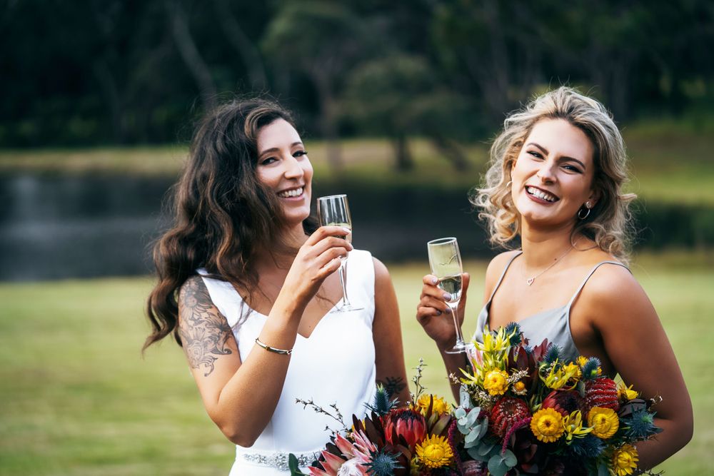 Wedding party smiles and laughs while holding bouquets with bright sunflowers in an outdoor setting.
