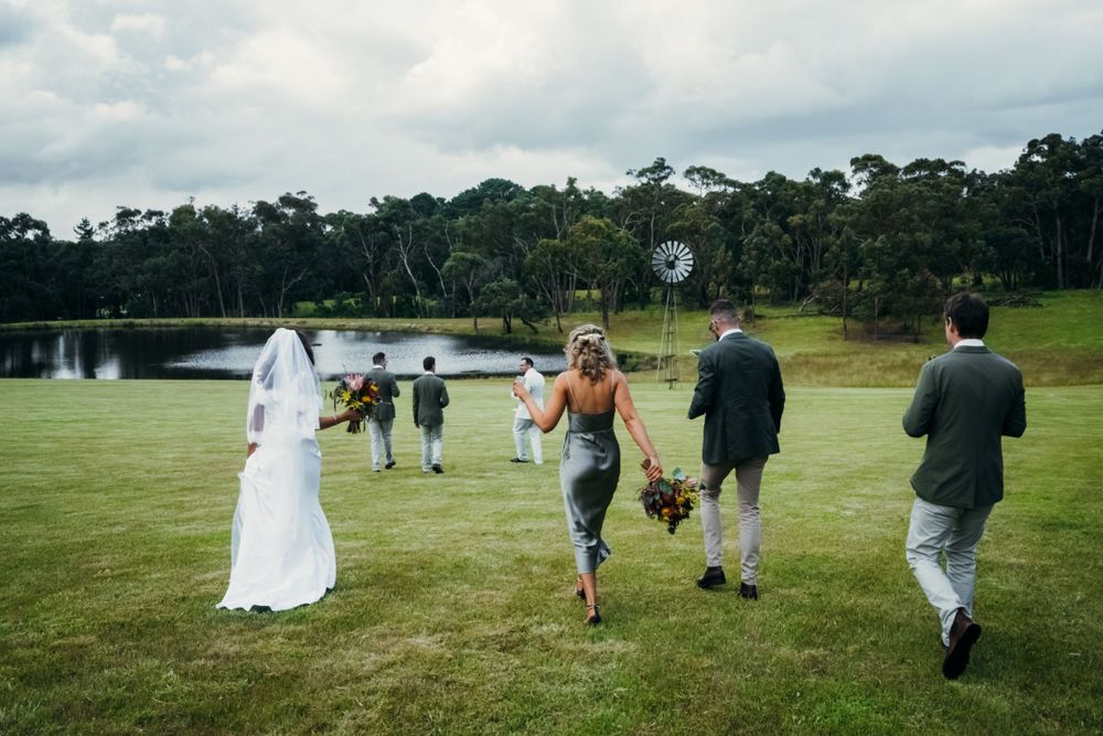 Wedding party walking across a scenic grassy field on an overcast day.