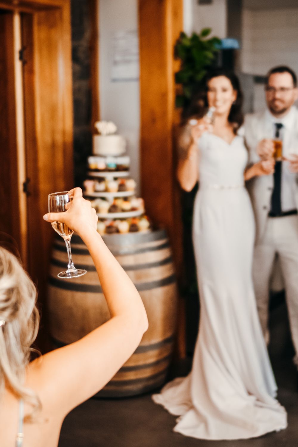 Reception venue decorated with wooden barrels and white wedding cake in rustic indoor setting.