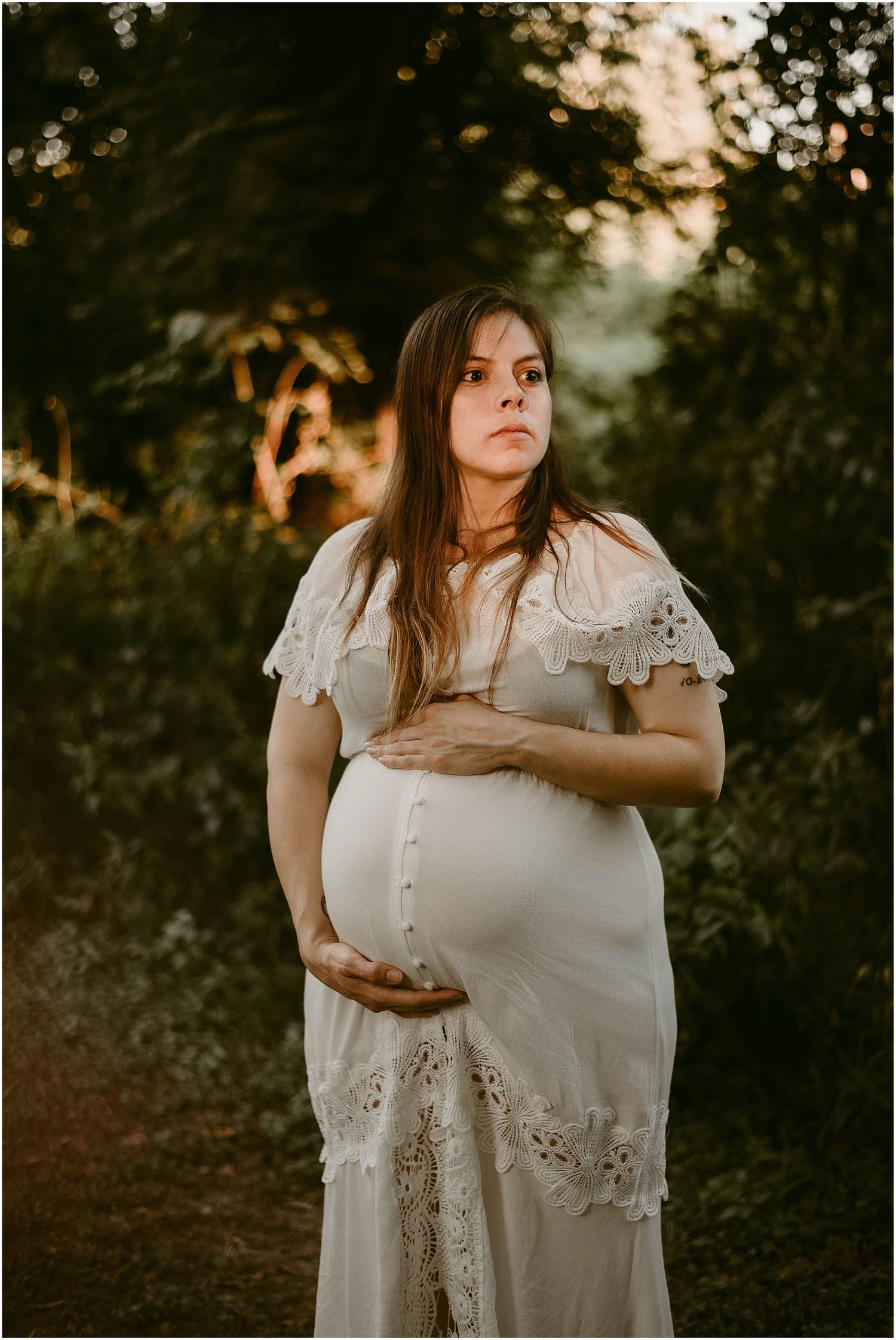 Dramatic sunset maternity portrait with golden backlighting through trees.