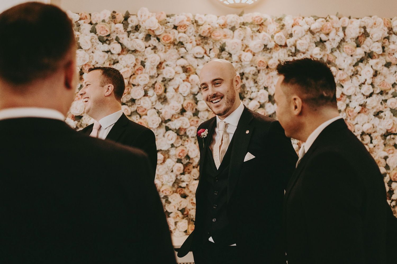 Wedding celebration scene with floral wall backdrop and formal attire.