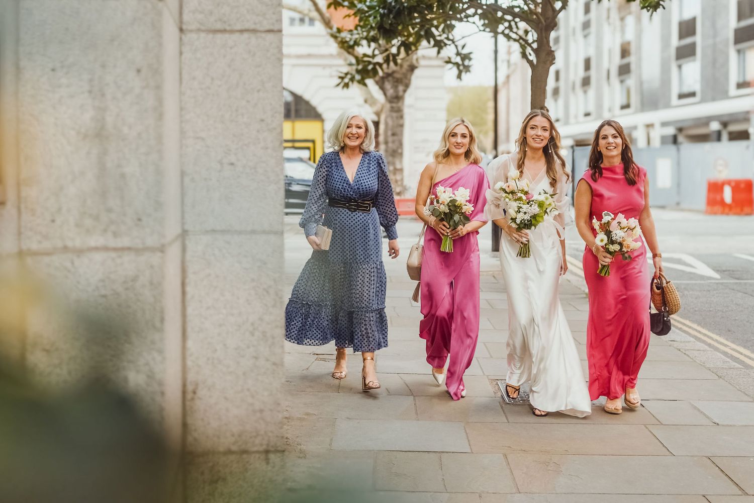 Wedding party walking down street with bridesmaid dresses in shades of pink and purple.